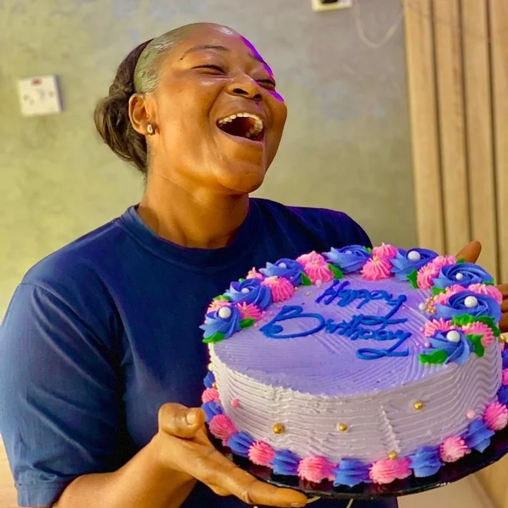A smiling woman holding a colourful celebration cake